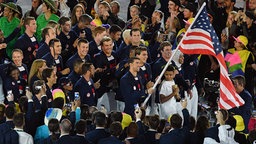 Michael Phelps leitet sein Team mit der US-amerikanischen Flagge ins Stadion. © dpa picture alliance Foto: Lukas Schulze