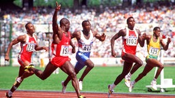 Ben Johnson jubelt über seinen 100-m-Sieg bei Olympia 1988. Später wird er wegen Dopings disqualifiziert. Carl Lewis (2.v.r.) erhält Gold. © picture-alliance / Sven Simon