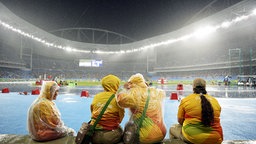 Helfer sitzen im Regen im Stadio in Rio. © dpa Foto: Franck Robichon