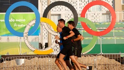 Jogger passieren die Olympischen Ringe am Copacabana Strand während der Olympischen Spiele © dpa - Bildfunk