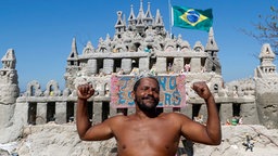 Ein Mann posiert vor einer Sandburg am Praia do Pepe Strand in Rio de Janeiro © dpa Foto: Javier Etxezarreta