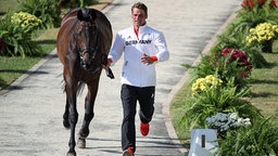 Vielseitigkeitsreiter Andreas Ostholt läuft neben seinem Pferd So is et. © dpa bildfunk Foto: Friso Gentsch