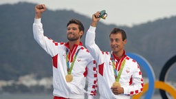 Die kroatischen Segler Sime Fantela (l.) und Igor Marenic zeigen ihre Goldmedaillen. © dpa Foto: Oliver Hoslet