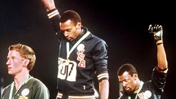 Die Amerikaner Tommie Smith (M., Goldmedaille) und John Carlos (r., Bronzemedaille) demonstrieren während der Olympischen Spiele 1968 bei der Siegerehrung für den 200-m-Lauf der Männer für die "Black Power"-Bewegung. © picture-alliance/ dpa 