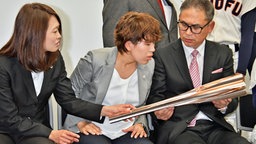 Japanische Sportler betrachten die Fackel für die Olympischen Spiele in Tokio 2020. © imago images / AFLOSPORT 