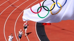 Im Olympiastadion von London 2012 messen sich Läufer unter einer Fahne mit den Olympischen Ringen. © imago images / Laci Perenyi 