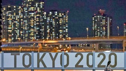 Eine Frau geht bei Nacht am Schiftzug "Tokyo 2020" vorbei. © dpa-Bildfunk 