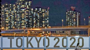 Eine Frau geht bei Nacht am Schiftzug "Tokyo 2020" vorbei. © dpa-Bildfunk 