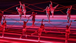 Tänzer und Tänzerinnen halten rote Fäden © imago images/Agencia EFE Foto: Enric Fontcuberta