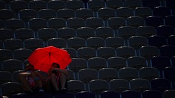 Zwei britische Athleten sitzen während des Mannschaft-Wettbewerbs auf der Tribüne unter einem roten Schirm. © dpa-Bildfunk Foto: Marijan Murat/dpa