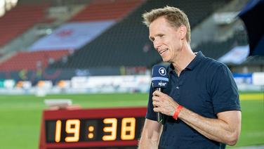 ARD-Leichtathletik-Experte Frank Busemann steht mit einem Mikrofon in der Hand in einem Stadion. © picture alliance / SVEN SIMON Foto: Anke Waelischmiller