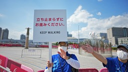 Ein Mitarbeiter hält ein Schild mit der Aufschrift "keep walking" hoch und fordert mit einem Kollegen durch Gestik zum Weitergehen auf. © picture alliance/dpa Foto:  Michael Kappeler