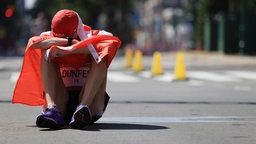 Evan Dunfee aus Kanada sitzt nach dem Bronzesieg im 50km Gehen von den Emotionen und der Erschöpfung überwältigt auf dem Boden  © dpd-bildfunk Foto: Eugene Hoshiko