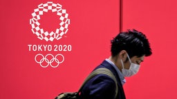 Ein Mann mit Mund-Nasen-Schutz geht an einem Werbeplakat für die Olympischen Spiele in Tokio vorbei.  