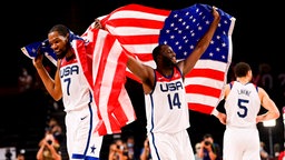 Die US-amerikanischen Basketballer Kevin Durant (l.) und Draymond Green bejubeln den Olympiasieg mit Flaggen. © IMAGO / PanoramiC