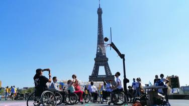 Menschen in Rollstühlen spielen Basketball vor dem Eifelturm in Paris. © IMAGO / PanoramiC 