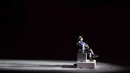 Ein Künstler sitzt im Lichtkegel zum Anfang der Zeremonie © IMAGO / SNA Foto: Pavel Bednyakov